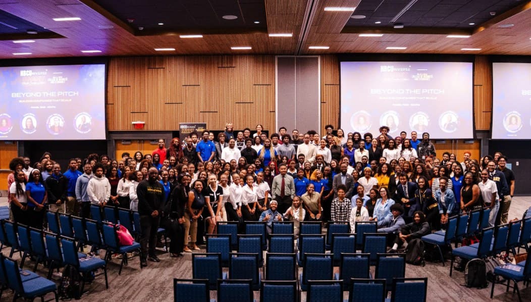 A full conference room of students and attendees posing together at a Venture for T.H.E.M. event.